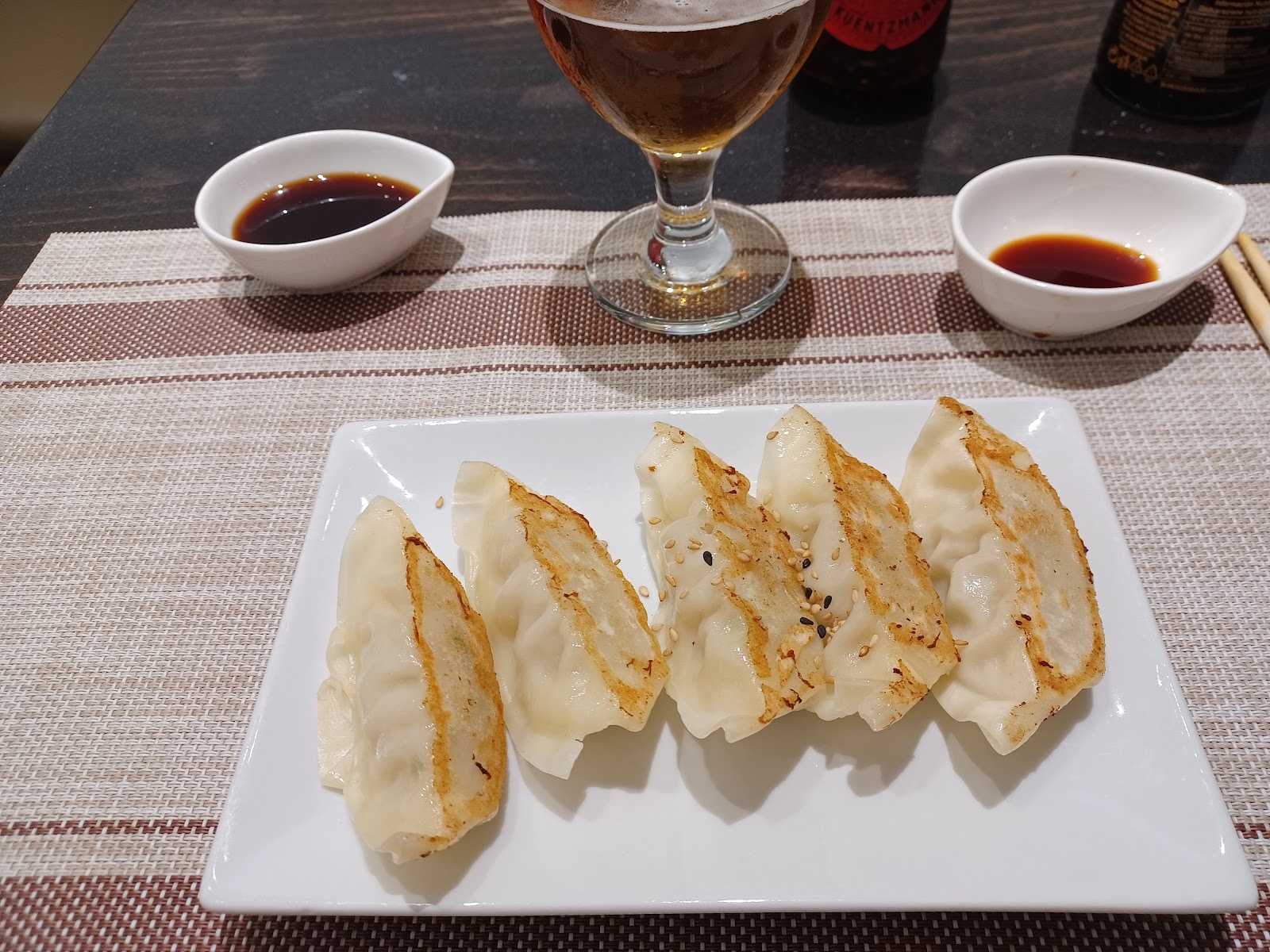 Five pan-fried dumplings on white plate with soy sauce and beer